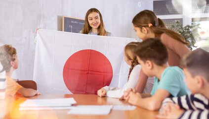 Kindly pedagogue demonstrating Japan flag to preteen pupils in teaching room during class