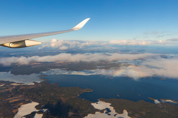 Flying above the clouds. View of clear blue sky, airplane wing and lakes and land on a sunny day.