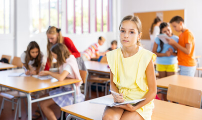 Sad bored schoolgirl sitting separately in classroom in break between lessons