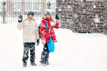 Two teenage friends stand side by side in the middle of a snowfall