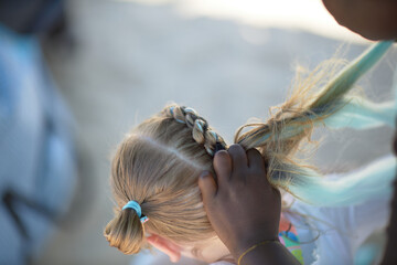 holding braids with pink color on little kid head. stylist applying braiding hair on young baby.