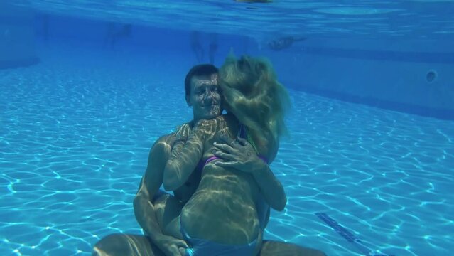 Woman sit on man cuddling under water of swimming pool and man touch woman ass