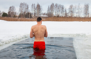 a man swims in an ice hole during winter swimming, winter therapy, ice bathing in the river, hardening the body and soul, body energy!
