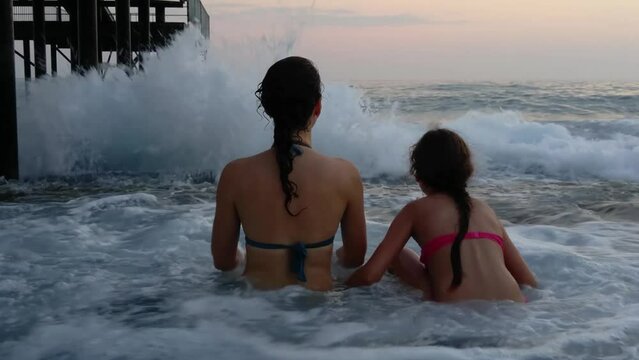 Backs of mother and daughter in swimming suits jumping on seaboard