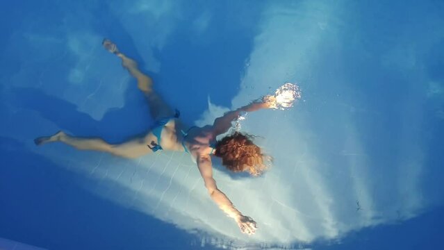 Back of woman diving spreadeagle on bottom of swimming pool in light