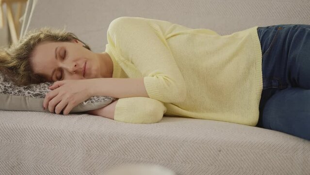 Woman at home, lying on couch in living room, napping, sleeping, resting. Adult caucasian woman in 30s .