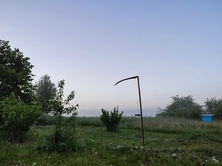 an antique scythe stuck in a freshly mown green field on an early summer morning
