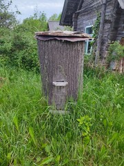 an old abandoned beehive made from a tree trunk stands on a field near a barn in the village