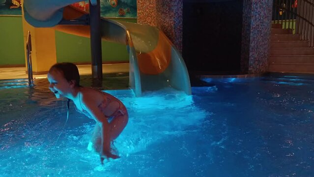 Children in the water park slide down the slide into the water, rejoice and splash on vacation