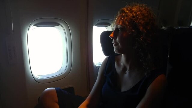 Woman sit near illuminator and emergency exit of flying airplane in twilight