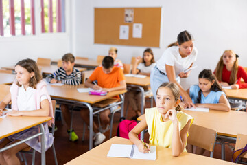 Children sitting at lesson in classroom, teacher standing