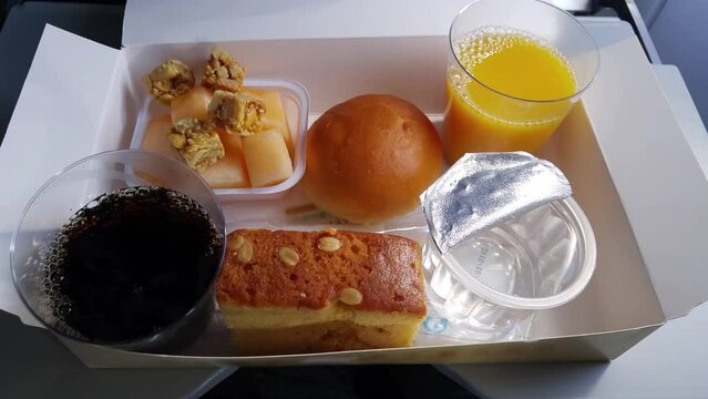 Cake, bread, sweet nuts, water, juice and black drinks in cups in airplane