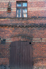 Wall of old brick house, Upper Silesia. Window, small statue, wooden door. Piekary Slaskie, Poland.