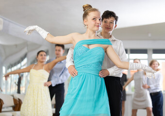 Enthusiastic friendly teenagers, boy and girl in party attire performing elegant waltz in pair in...