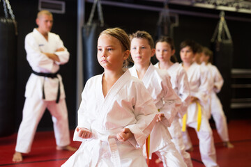 Young boys and girls in kimono doing kata moves with their trainer in gym.