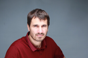 Obraz premium A picture of a man with a beard, mustache and fashionable hairstyle, dressed in a casual polo shirt, posing in a studio with a serious expression on a light background