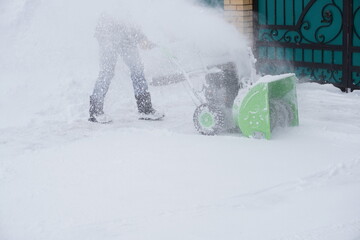 A man cleans snow in the winter in the courtyard of the house,  man cleaning snow with a snow blower