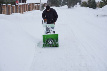 A man cleans snow in the winter in the courtyard of the house,  man cleaning snow with a snow blower