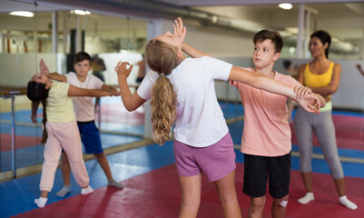 Positive kids in pair exercising self-defense movements during group class with female coach
