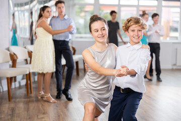 Fototapeta premium Teen guy and girl perform movements and dance hustle in pairs under guidance of woman coach. Classes in dance studio, choreography