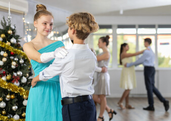 Positive teenage girl in festive dress dancing elegant slow ballroom dance with boy partner during...