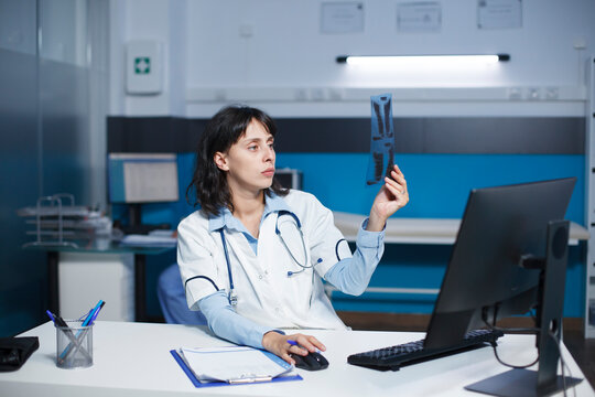 Dedicated doctor examining a CT scan of a patient, taking notes on desktop computer. The image shows caucasian female healthcare professional inspecting a chest X-ray image of an individual.