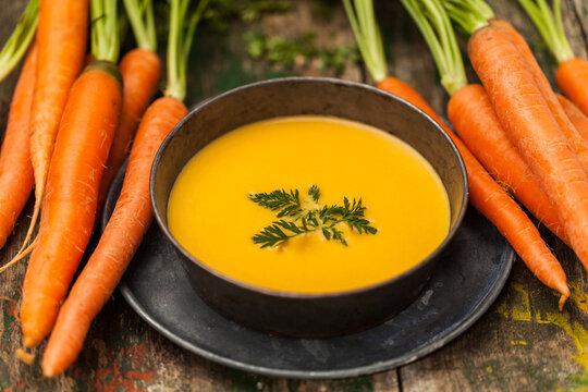 Carrot soup in a black bowl with fresh carrots