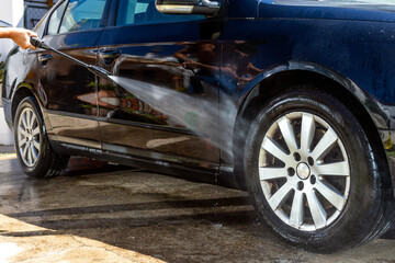 Man washing a car wheel rim with high pressure power washer gun at the carwash.