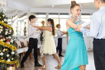 With unhurried music, teen boy and girl in couple spins to rhythm of tango during lesson for novice students in Christmas atmosphere. Classes in mini-groups for those who want to learn dancing