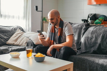 Man looking at his phone while watching sports on the couch