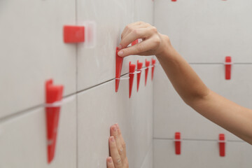 Woman tiling bathroom walls. Flat wall plastic tile leveling system. Process of installation of...