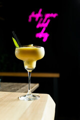 Vertical photo of a cocktail at a table inside a nightclub. The lemon cocktail is in a crystal glass. In the background is a neon pink. Modern cocktail concept. Advertising in cocktails.
