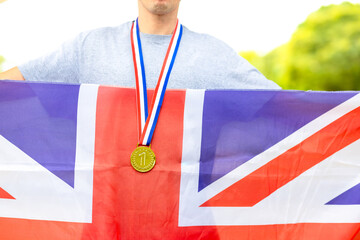 British male athlete proudly showcases a gold medal, symbolizing victory. Holding the Union Jack...