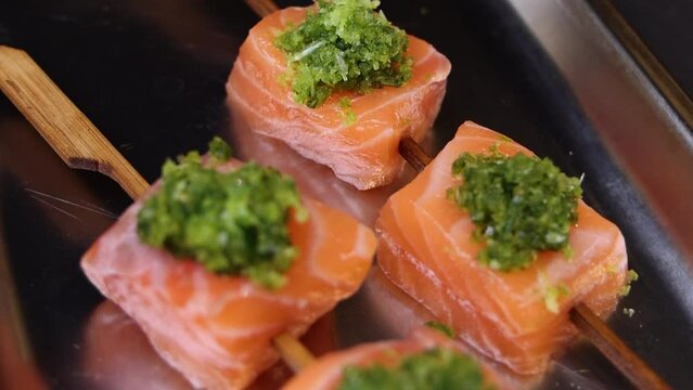 chef man hand is cutting salmon on blue board in restaurant, preparing dish for catering.cubes of fish with green spinach over ging in grill oven. close up from kitchen 4k