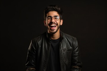 Portrait of a happy young man in leather jacket and eyeglasses over black background