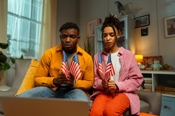 Sad supporters African American man and woman holding American flags, watching election results