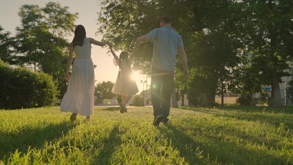 Happy family, kid, runs towards sun, holding hands in city park at sunset. Childhood future, family game. Slow motion. Family, mom dad daughter play together, active child jumps. Parents, kid nature