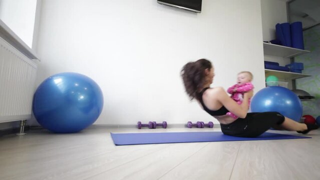 Young mother with daughter rolls on the mat with straight legs 