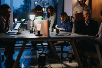 Team of multigenerational people collaborating at night. Diverse business colleagues in a warmly...