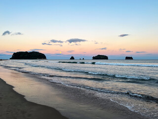 Whangamata Beach, where the sun gracefully sets, casting warm hues across the sky, and a full moon rises