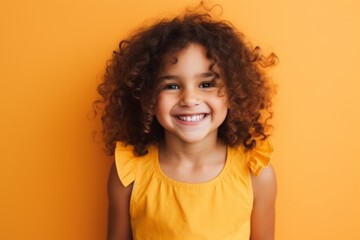 Portrait of a smiling little girl with curly hair over yellow background