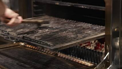 chef putting shrimp on wooden skewer and on charcoal grill oven. man cleaning rack with brush. fire flame and burning red embers inside. kitchen from a restaurant.hand using tongs to turn food