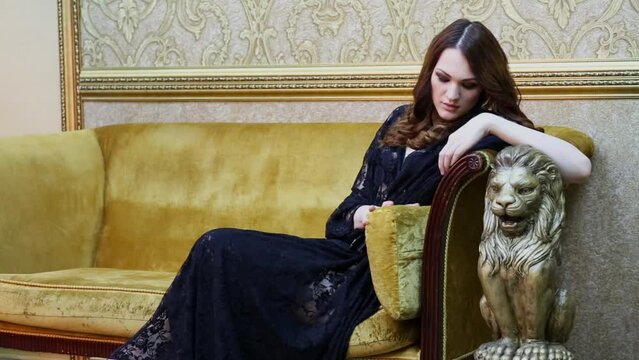 Brunette in black lace dress sits on sofa with yellow upholstery