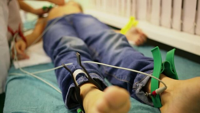 Nurse adjusts probes on young patient which lies on bed in hospital