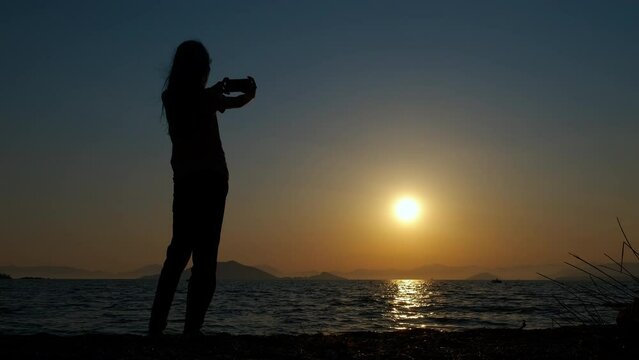 Teen silhouette makes sea photo. A young girl silhouette makes sunset photos on the beach during summer traveling.