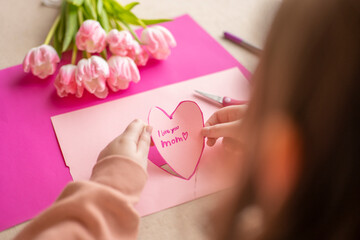 Obraz premium moms day. I love you, Mom. Childrens hands holding a heart card.Pink heart card and pink tulips.child makes a card for his mother.Flowers and cards for mom. 
