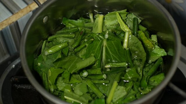 the process of boiling raw vegetables consisting of mustard greens and long beans which will be boiled and used as ingredients for making pecel dishes