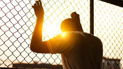Foto op Plexiglas Silhouette of a man behind the fence, Silhouette photo of  feeling upset, sad, unhappy or disappoint crying. Young people mental health care problem lifestyle concept, frustrated standing hopelessly © ภาคภูมิ ปัจจังคะตา