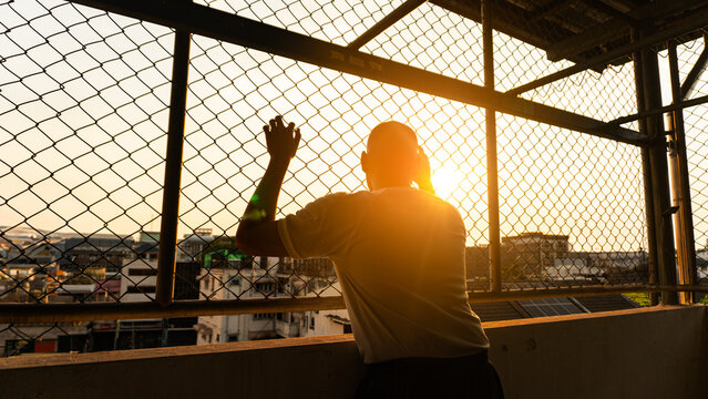 Silhouette of a man behind the fence, Silhouette photo of  feeling upset, sad, unhappy or disappoint crying. Young people mental health care problem lifestyle concept, frustrated standing hopelessly