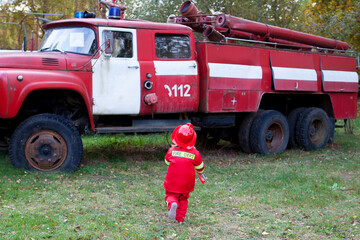 A little firefighter kid is running to the retro fire truck.